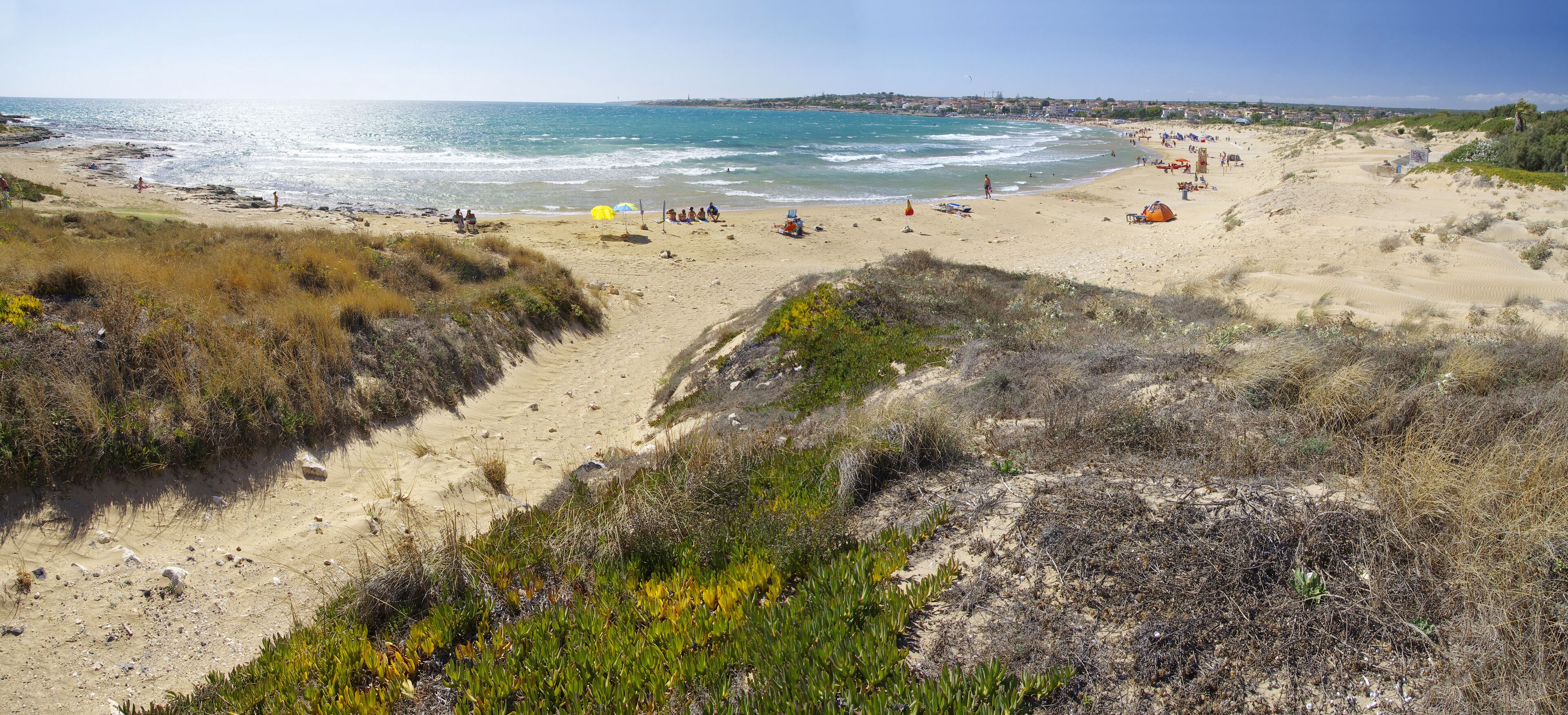 A coastal beach with dunes, beachgoers, and tents.