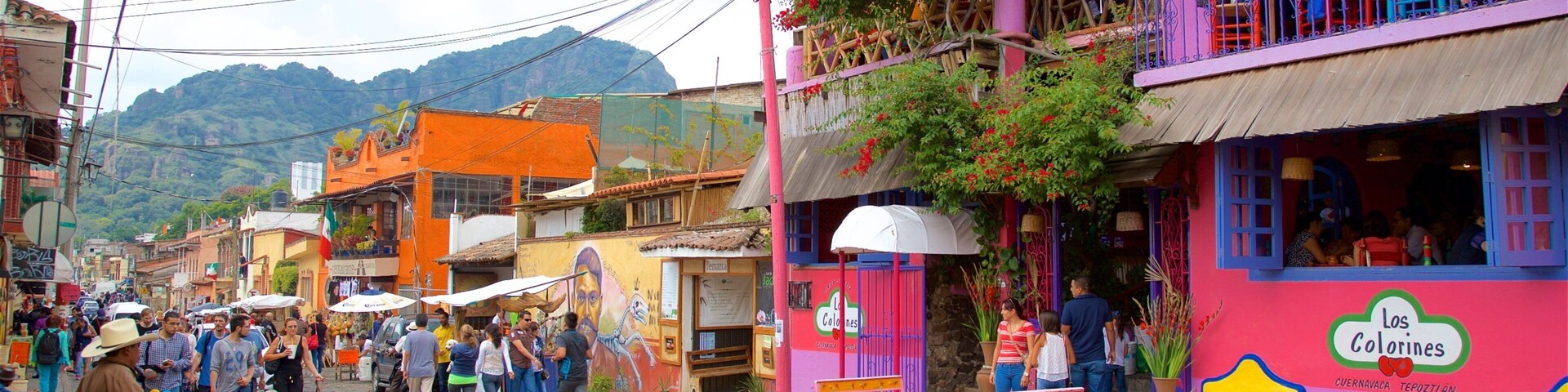 Uma rua colorida com pessoas caminhando, um cachorro e um prédio com a inscrição 'Los Colorines'.