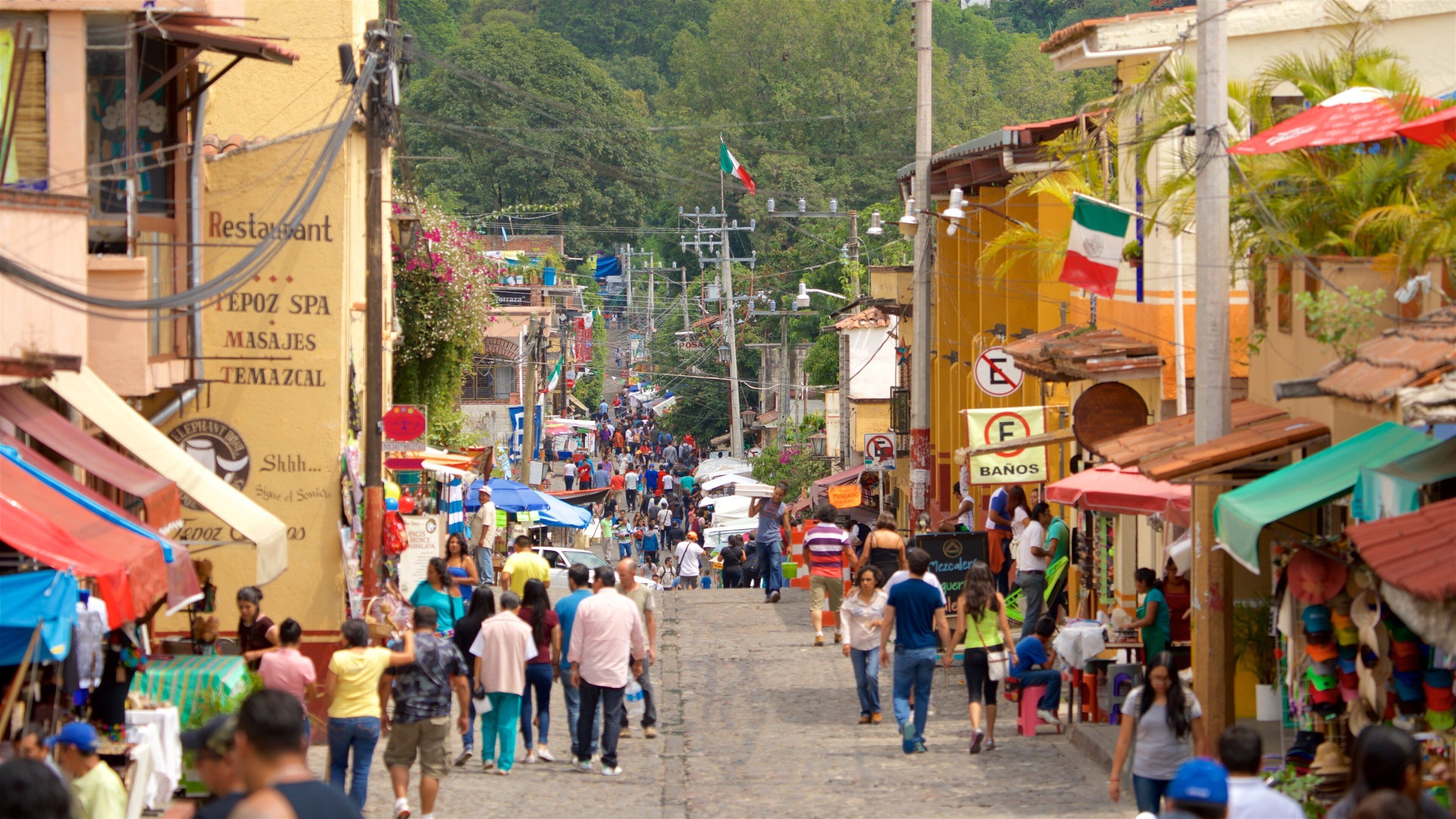 A bustling street in a mountainous town with shops and people walking.