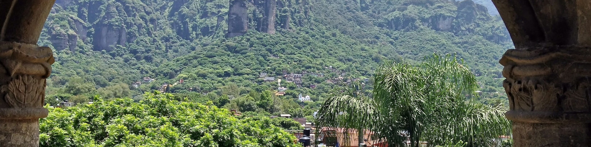 Vista a través de un arco de un paisaje verde exuberante con abundante follaje y una cadena montañosa distante.
