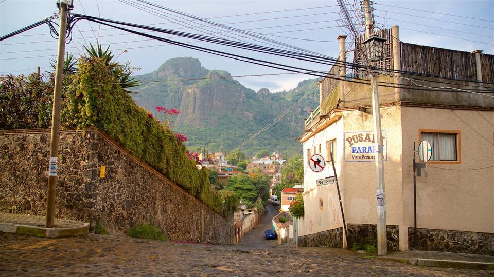 A narrow cobblestone street in a hilly town with a Posai Parati sign, a no right turn sign, and a view of mountains in the distance.