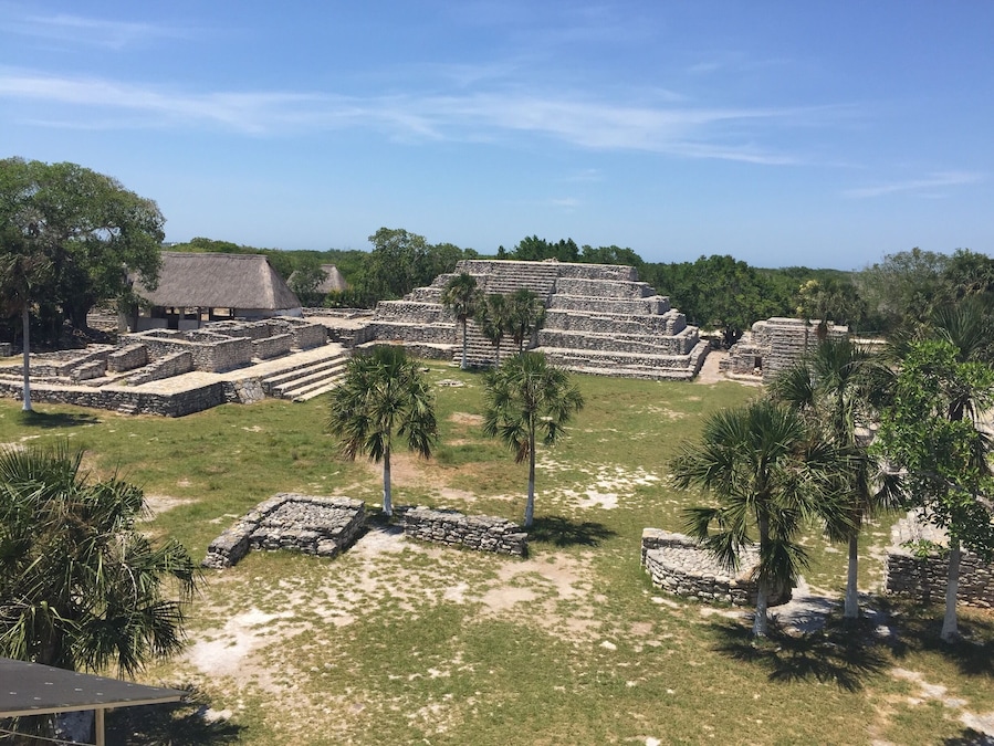 Ancient stone ruins with thatched-roof structures amidst lush greenery.