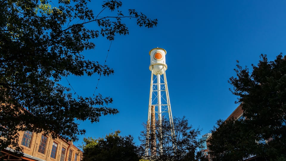 A water tower with a spherical orange top, surrounded by trees and a brick building.