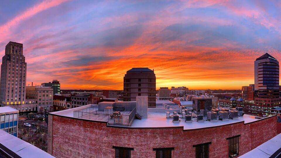 A cityscape at sunset with a prominent building in the center and a red brick building in the foreground.