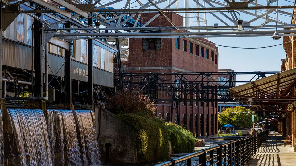 A water feature with a metal structure overhead, a brick building, and a pathway with railings.