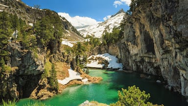 A mountainous landscape with a turquoise lake surrounded by snow-capped peaks and dense forests.