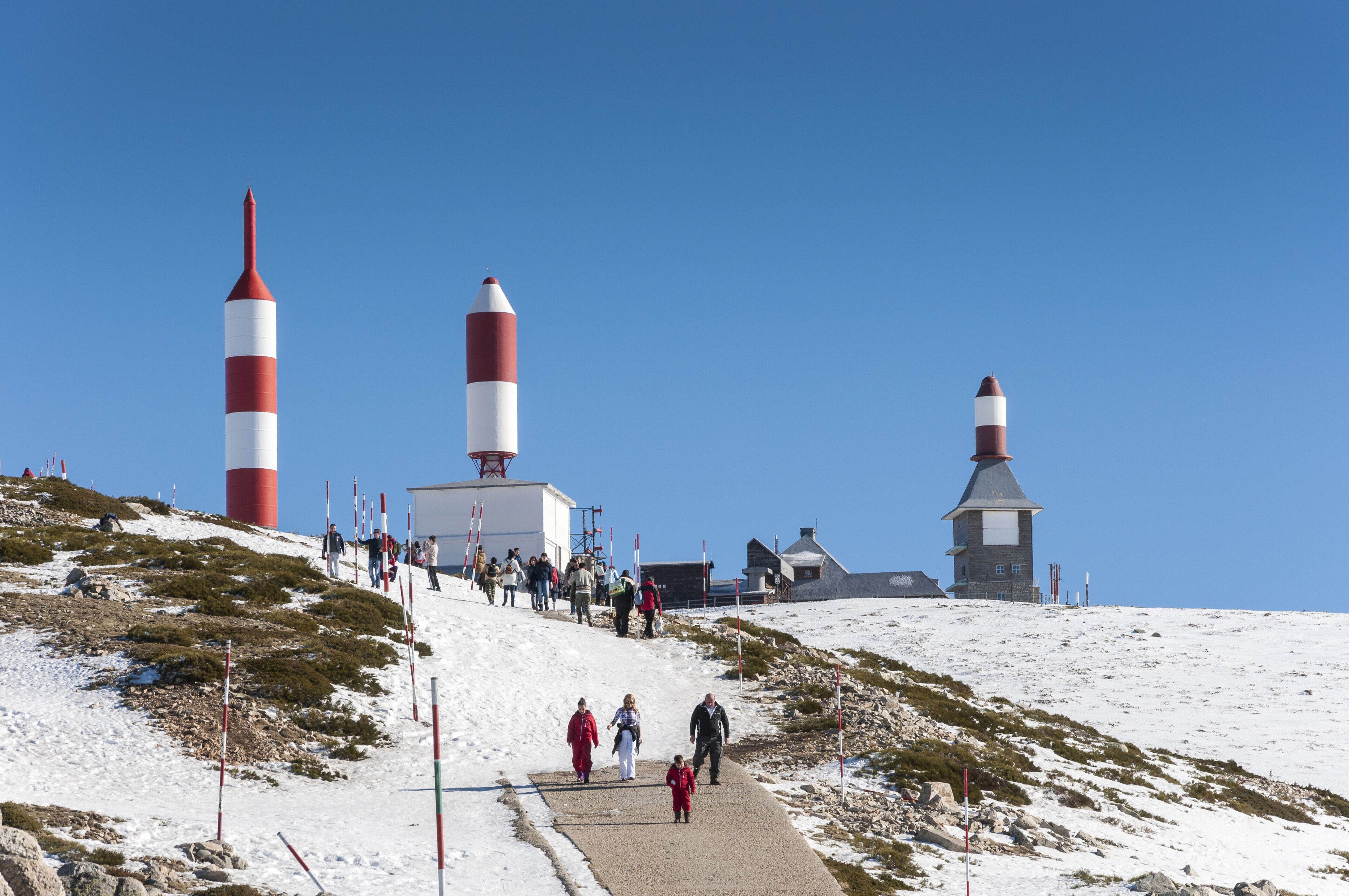 A snowy landscape with three lighthouses and a path with people walking.