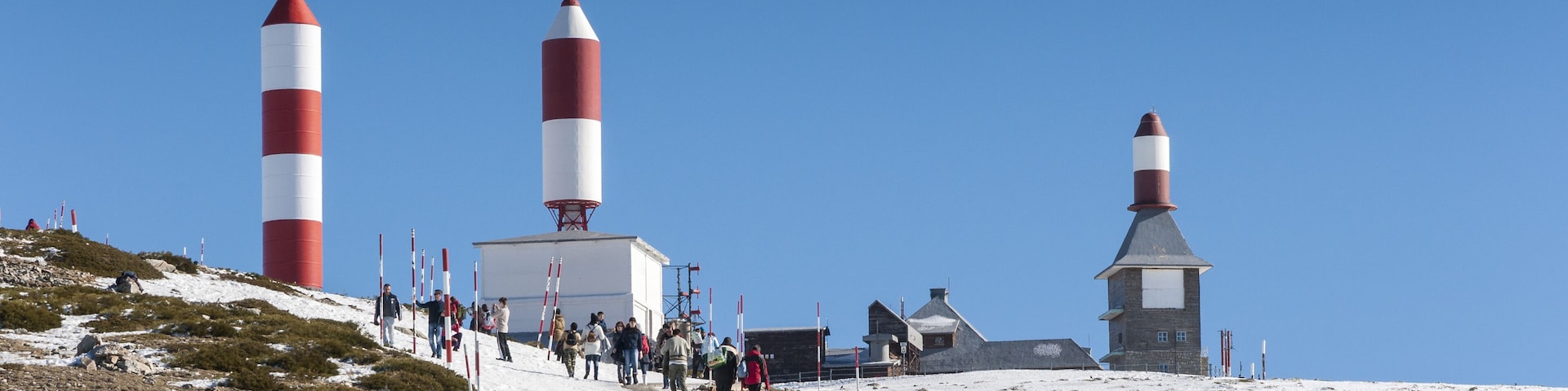 A snowy landscape with three lighthouses and a path with people walking.