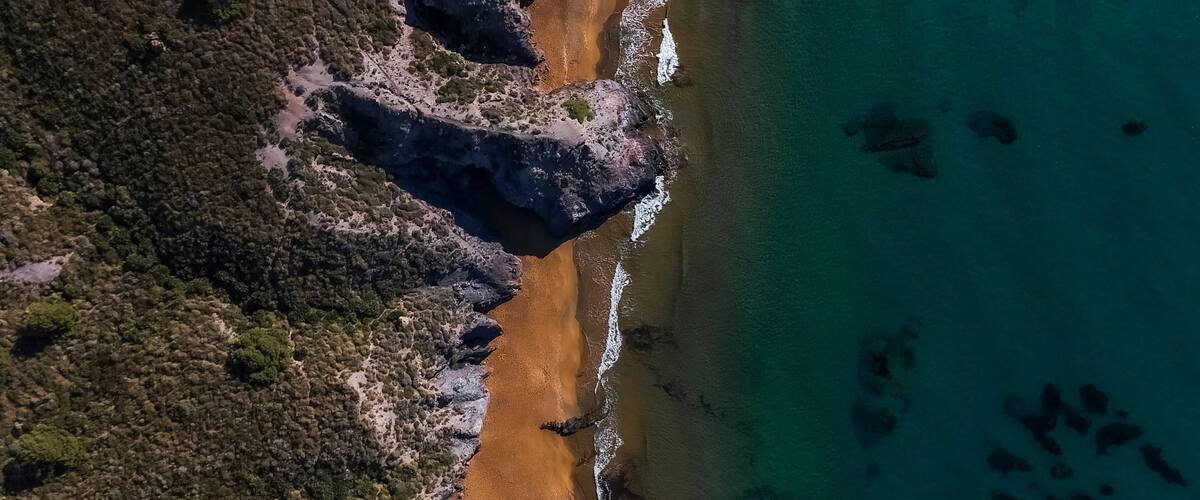 A coastal landscape with a sandy beach, rocky cliffs, and clear turquoise waters.