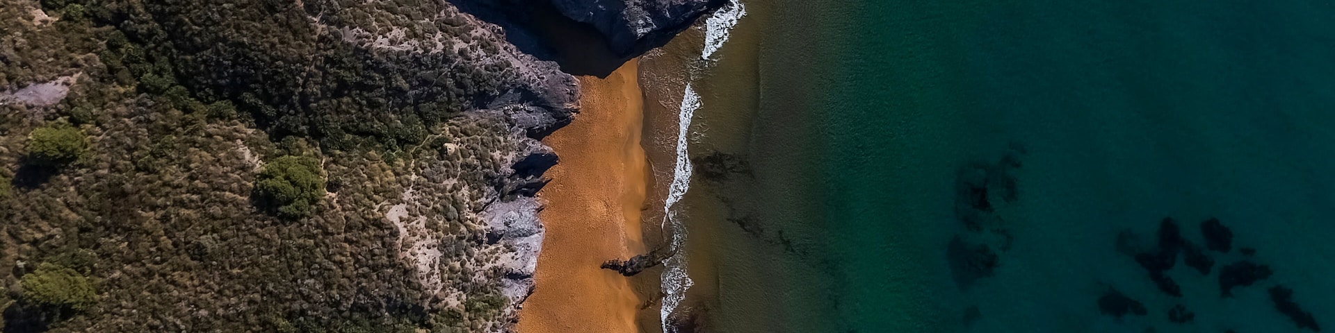 A coastal landscape with a sandy beach, rocky cliffs, and clear turquoise waters.