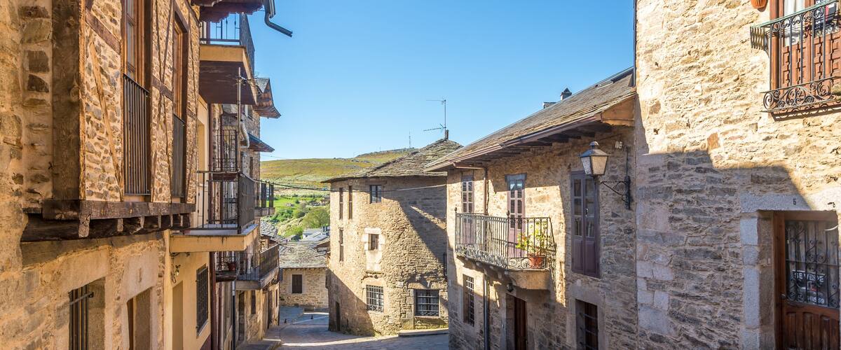 A narrow cobblestone street flanked by stone buildings with wooden shutters and balconies.