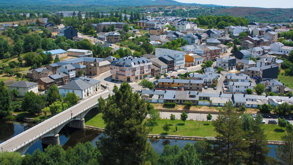 A town with a river, a bridge, and a hilly landscape in the background.