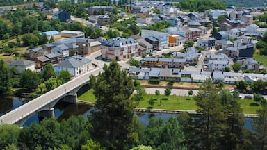 Un pueblo con un río, un puente y un paisaje montañoso al fondo.