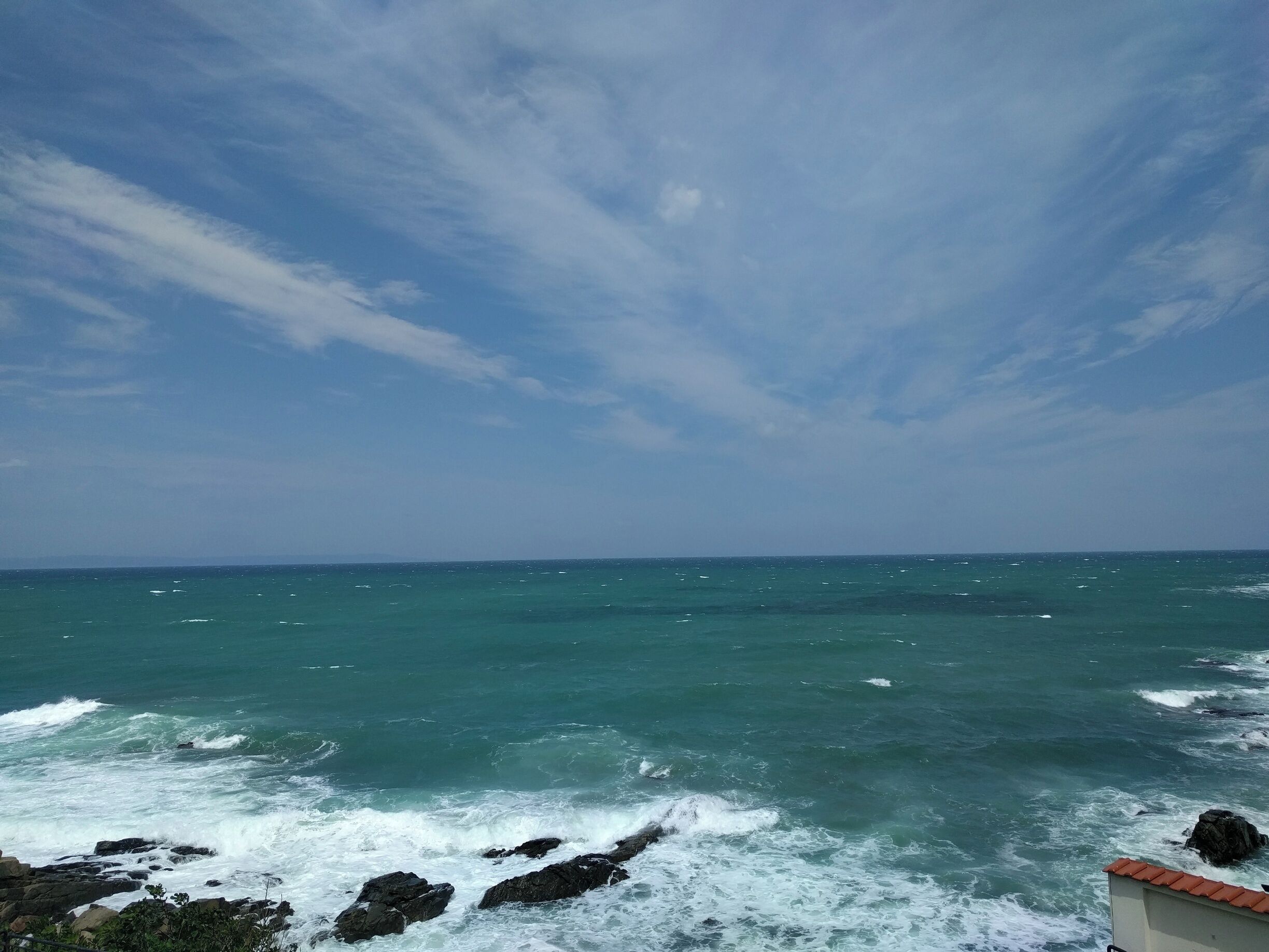 A coastal scene with waves crashing against rocks and a clear sky.
