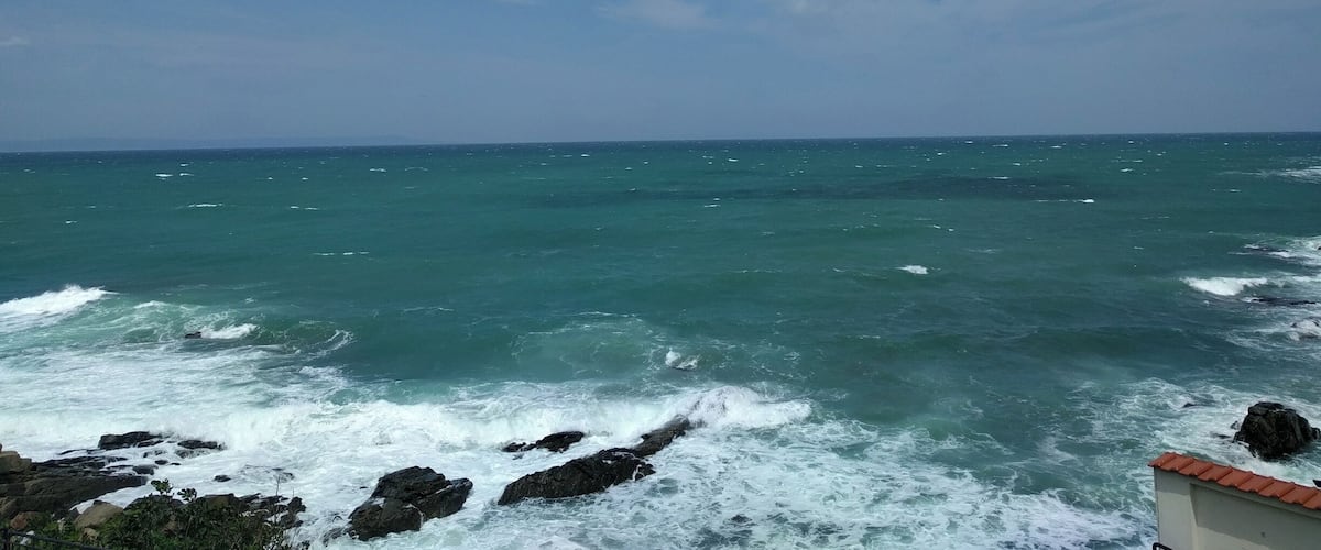 A coastal scene with waves crashing against rocks and a clear sky.