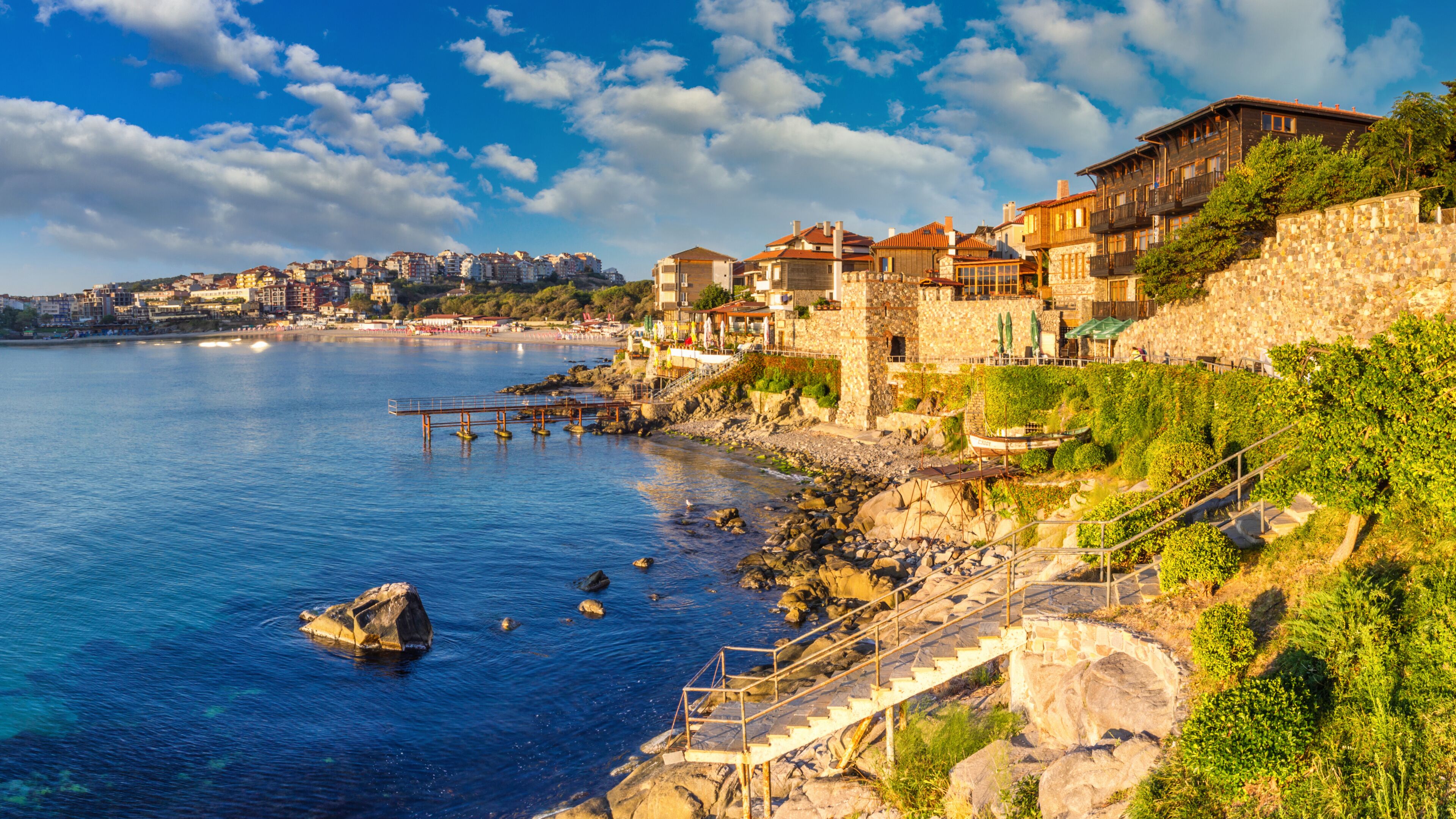 A coastal town with stone buildings, a pier, and a rocky shoreline.
