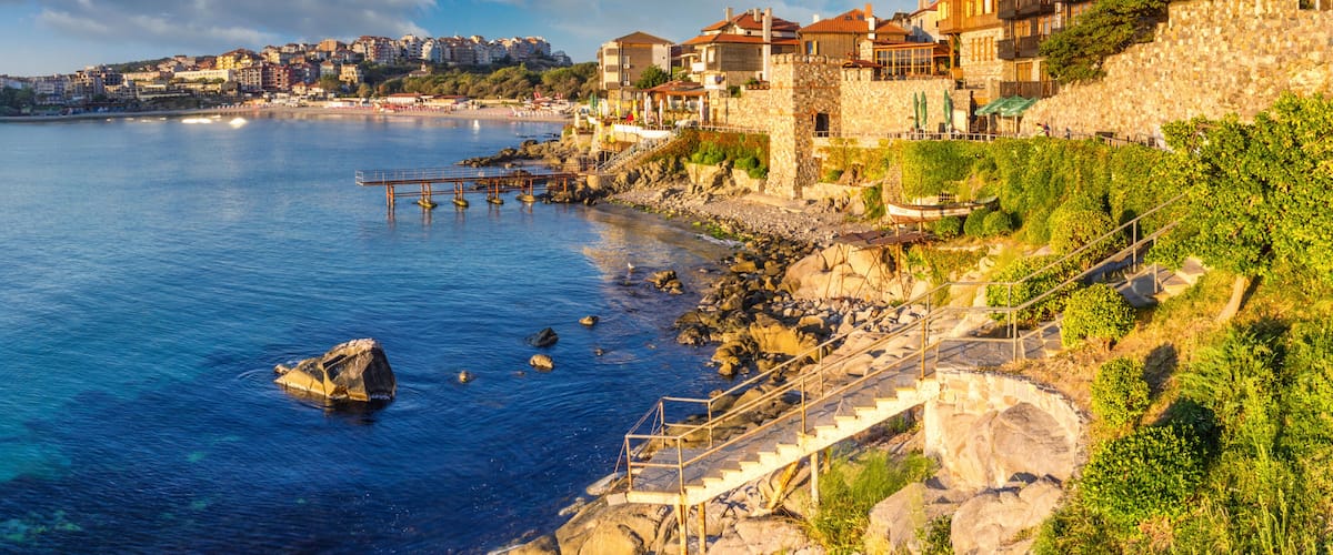 A coastal town with stone buildings, a pier, and a rocky shoreline.
