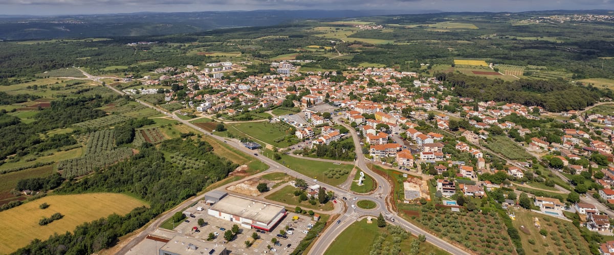 A town surrounded by green fields and mountains under a cloudy sky.