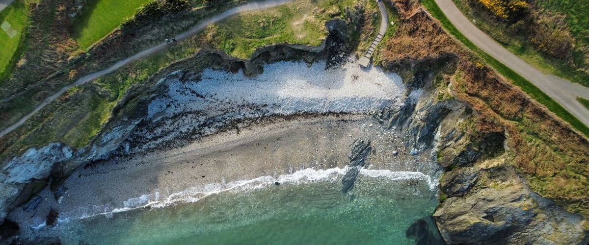 An aerial view of a coastal area with a sandy beach, rocky cliffs, and a clear blue sea.