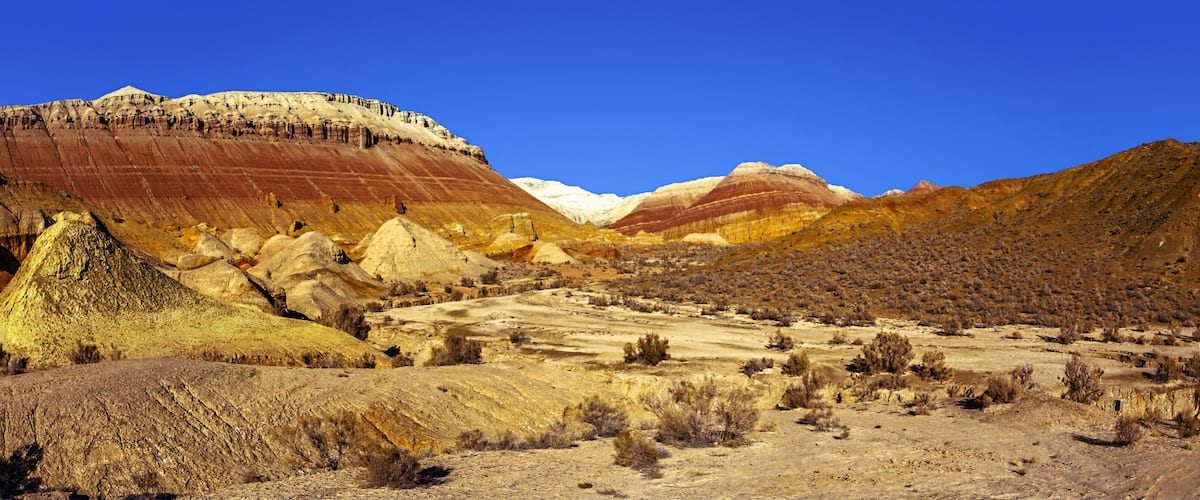 A colorful landscape with layered rock formations and sparse vegetation.