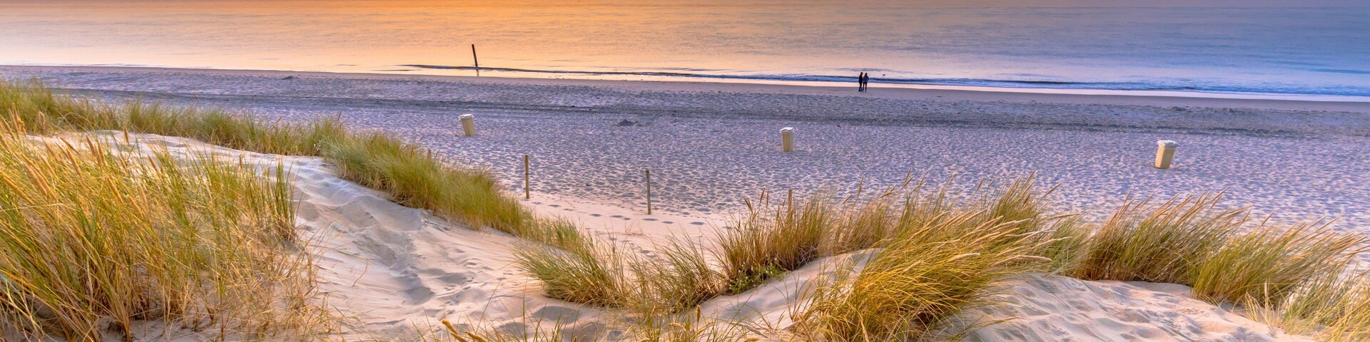 Uma praia com dunas de areia e uma pessoa caminhando ao longe.