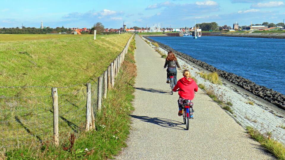 A paved path alongside a river, with a fence on one side and a rocky embankment on the other.
