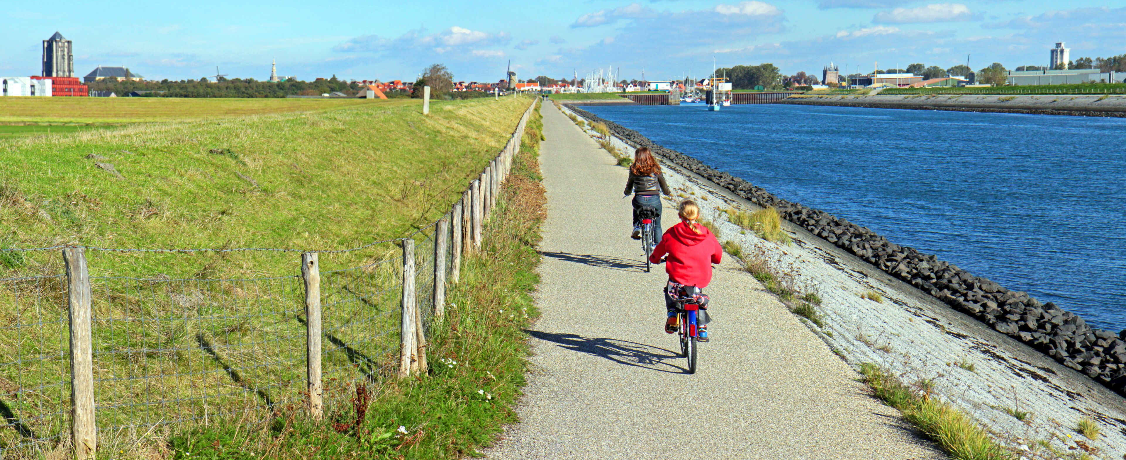 A paved path alongside a river, with a fence on one side and a rocky embankment on the other.