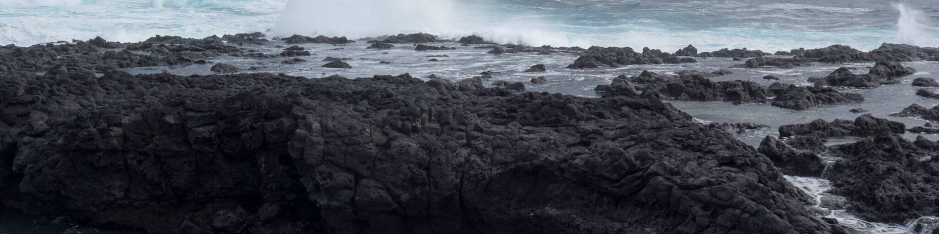 Une côte rocheuse où des vagues déchaînées s’écrasent contre les rochers.
