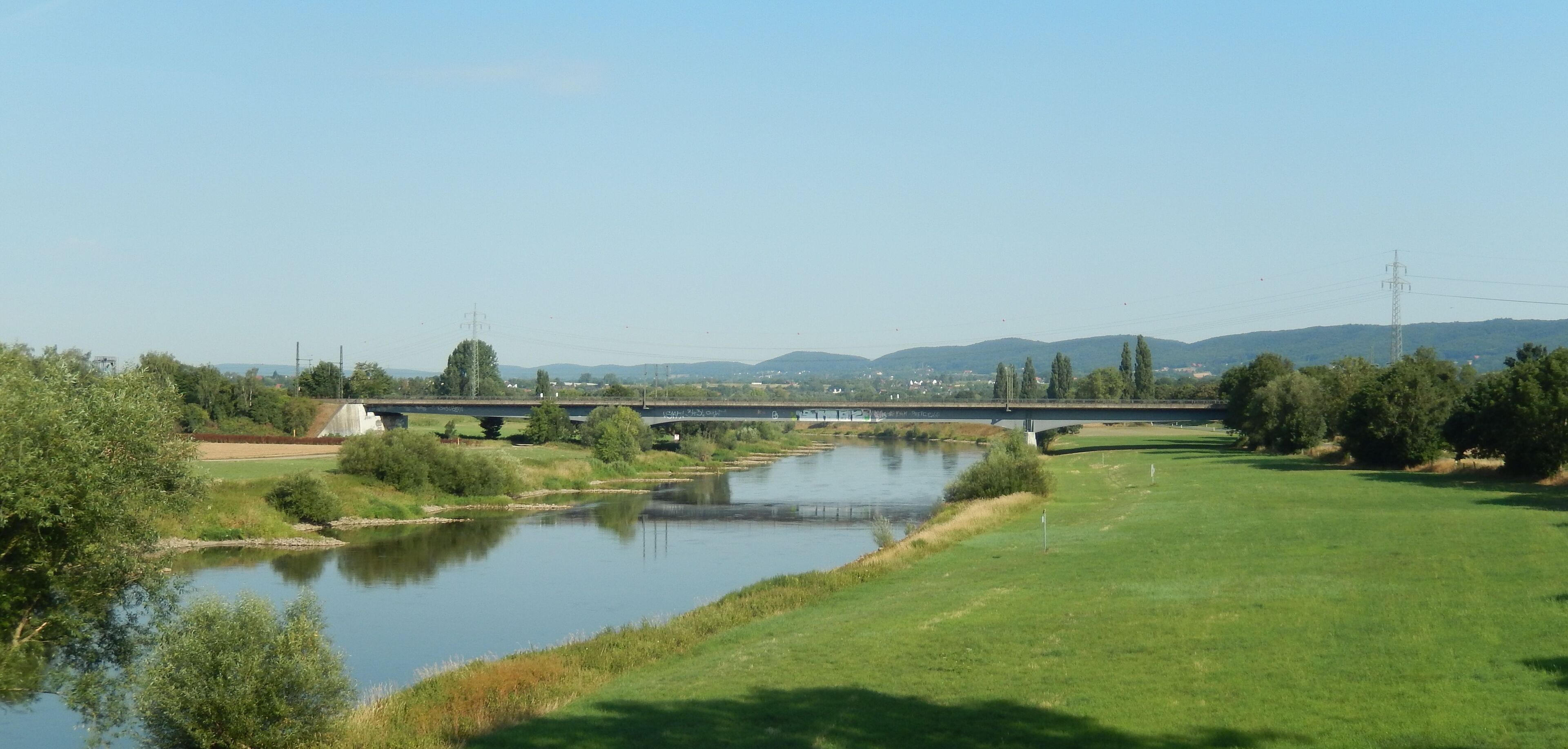 A bridge over a river with surrounding greenery and distant hills.