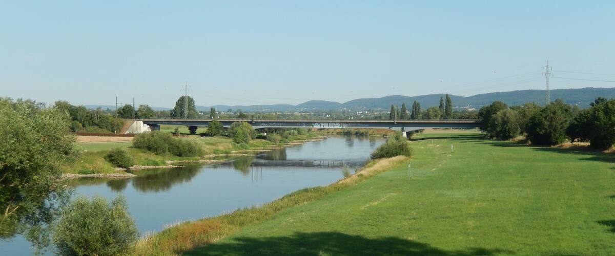 A bridge over a river with surrounding greenery and distant hills.
