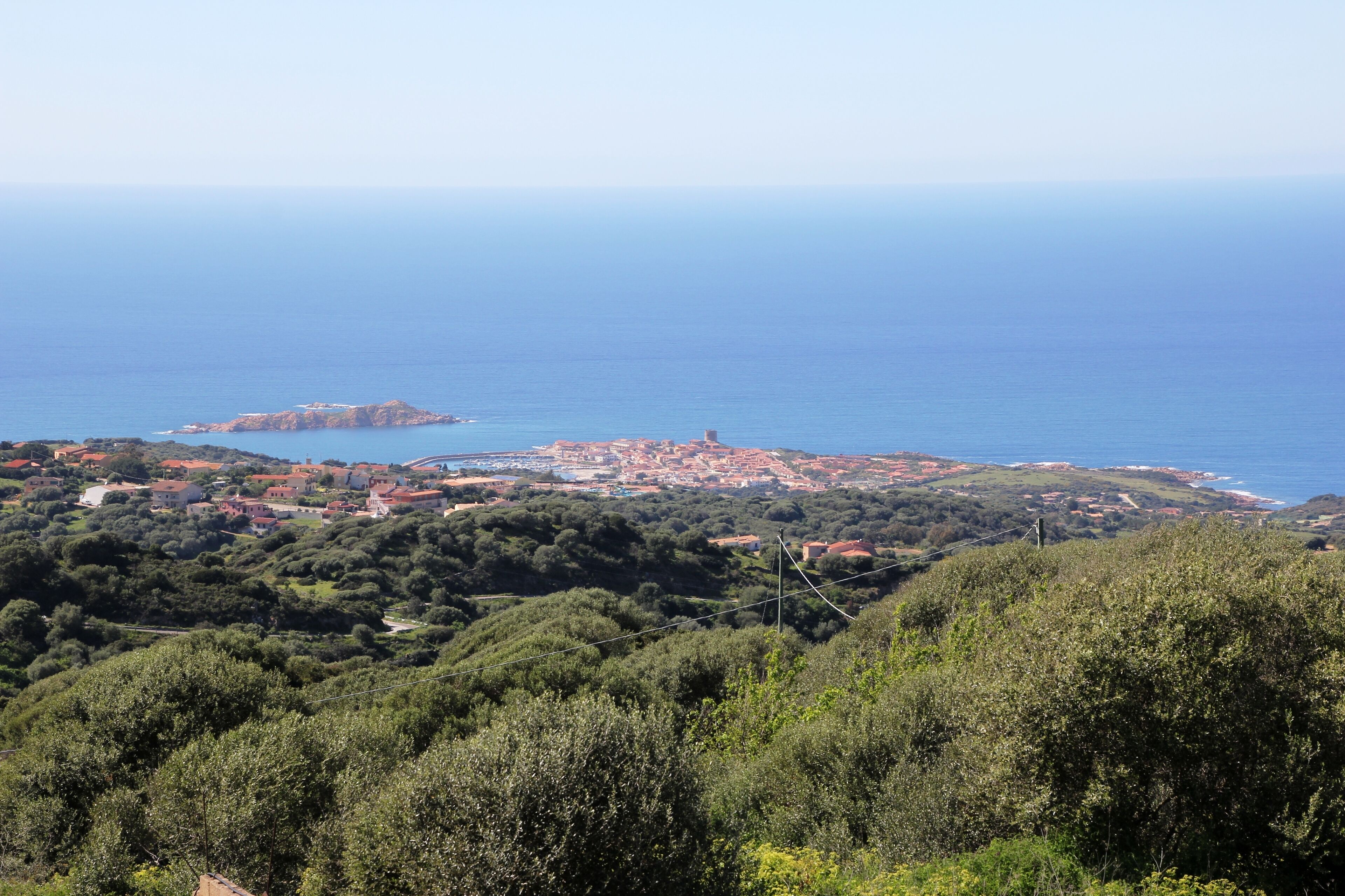 Un pueblo costero con edificios de techo rojo, una pequeña isla y colinas verdes exuberantes.