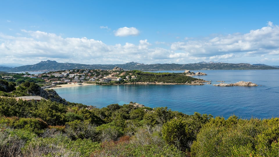 A coastal town with a bay, surrounded by mountains and dense greenery.