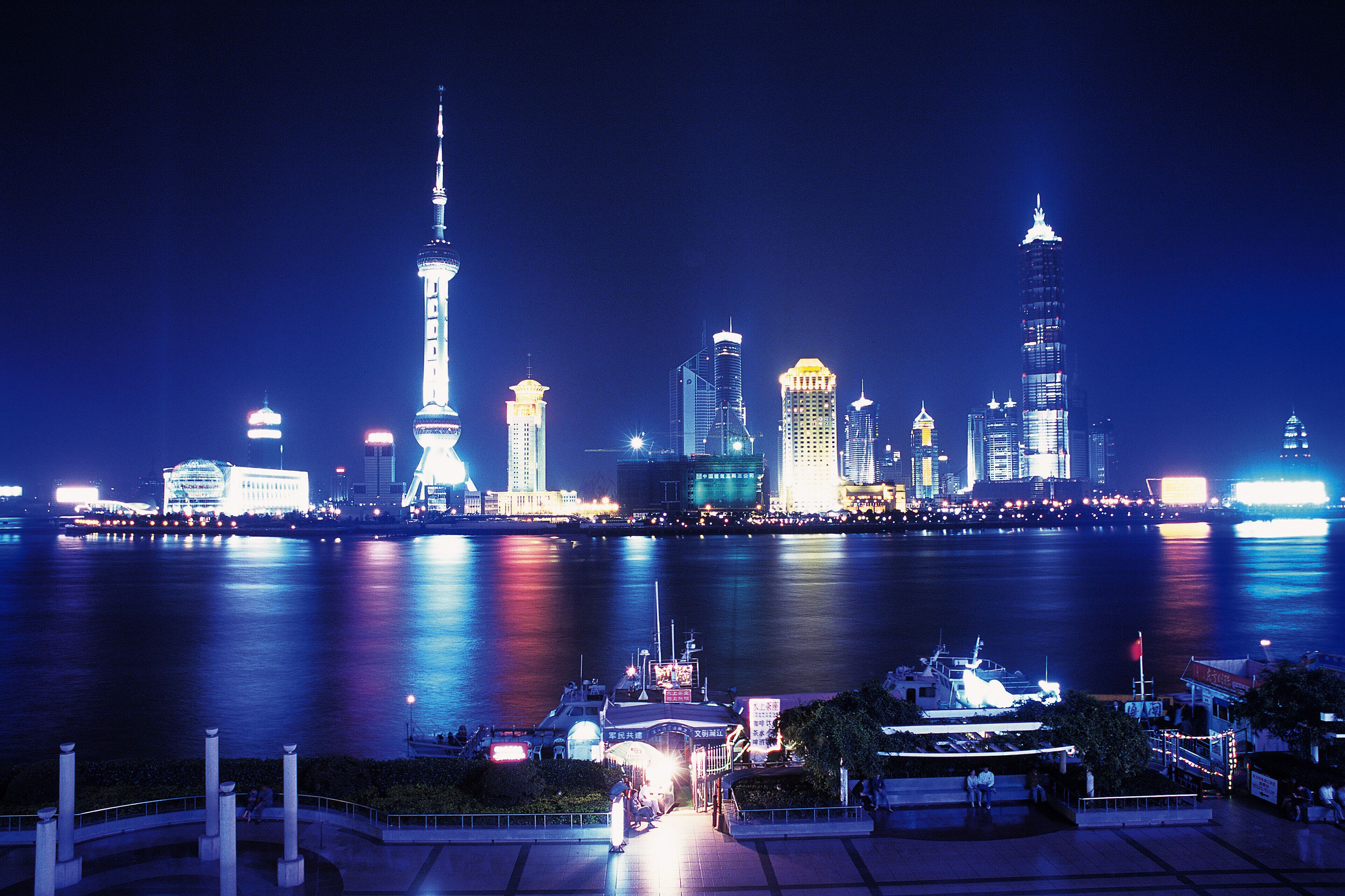 A nighttime city skyline with illuminated buildings and a river reflecting the lights.