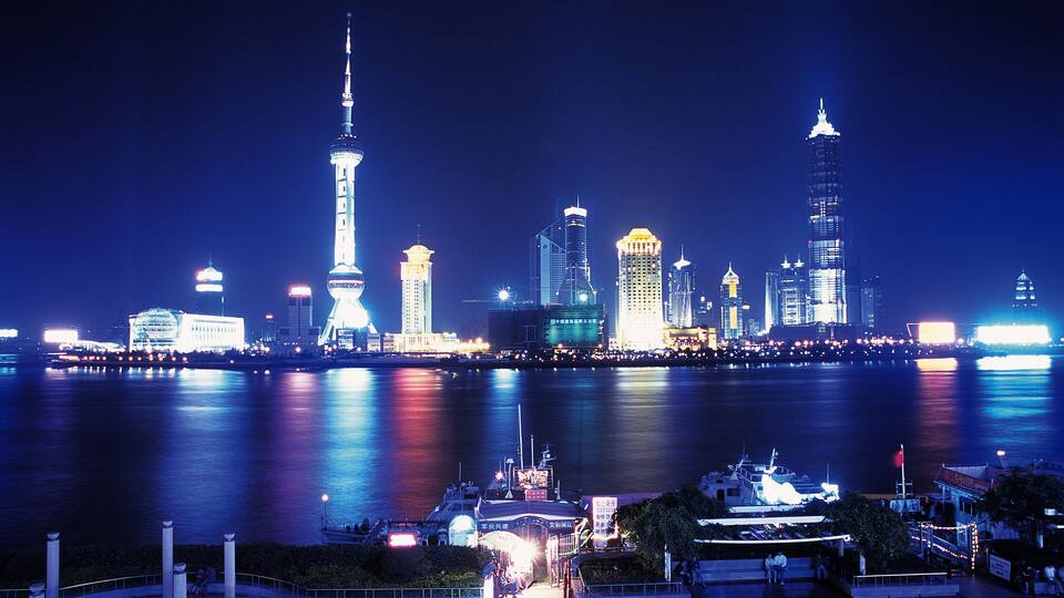 A nighttime city skyline with illuminated buildings and a river reflecting the lights.