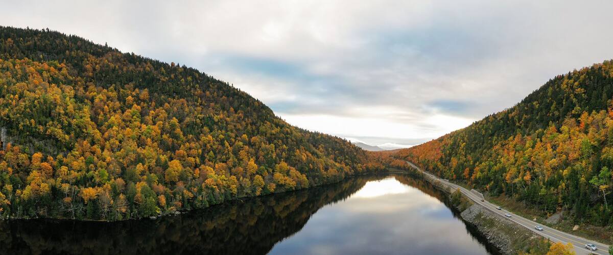 A river flanked by forested hills with autumn foliage.
