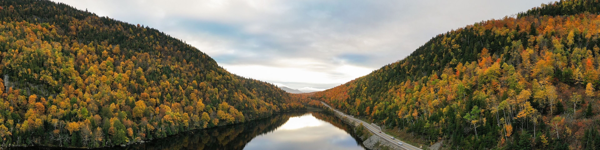 A river flanked by forested hills with autumn foliage.