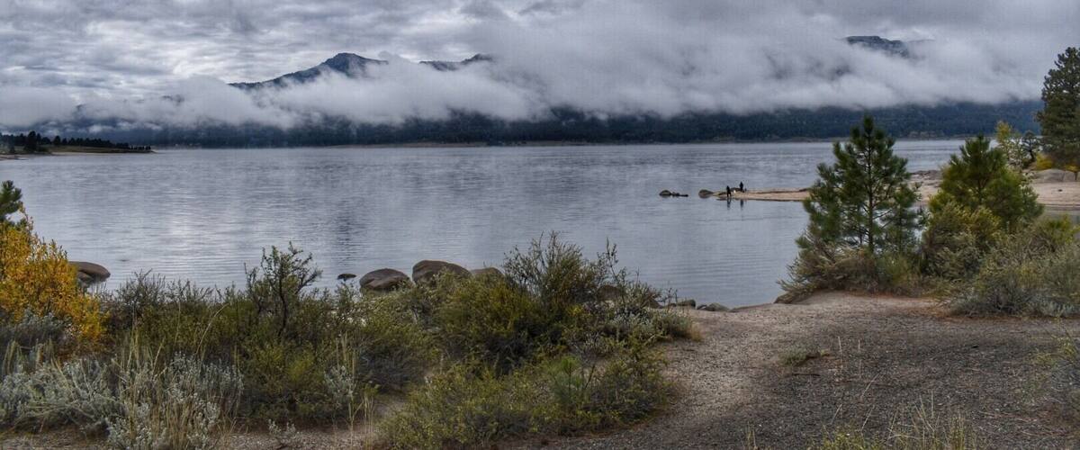 A lake with mountains in the background, surrounded by vegetation.
