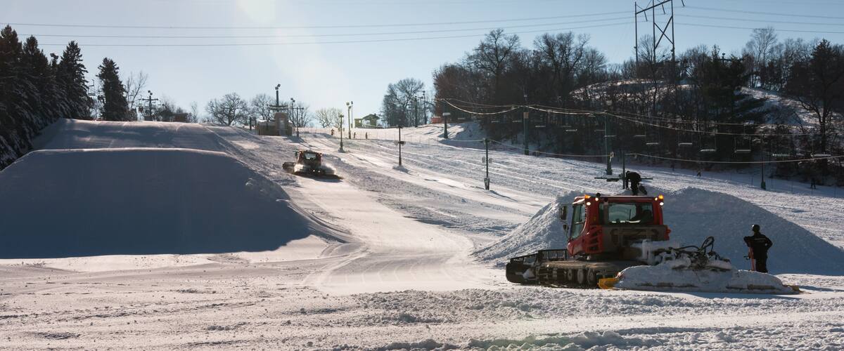 A snowplow clearing a road in a snowy landscape with a ski lift in the background.