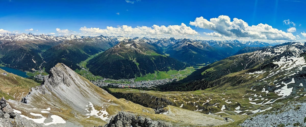 A mountain range with snow-capped peaks, a valley with a town, and a clear blue sky.