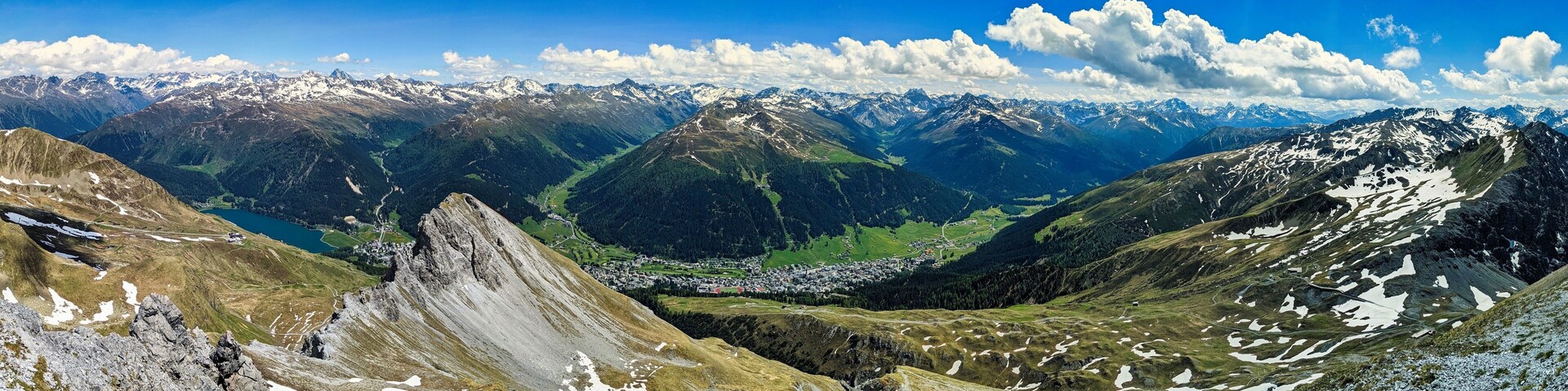 A mountain range with snow-capped peaks, a valley with a town, and a clear blue sky.