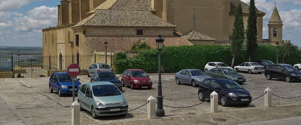 A historic building with a tiled roof and a tower, surrounded by parked cars and a clear sky.