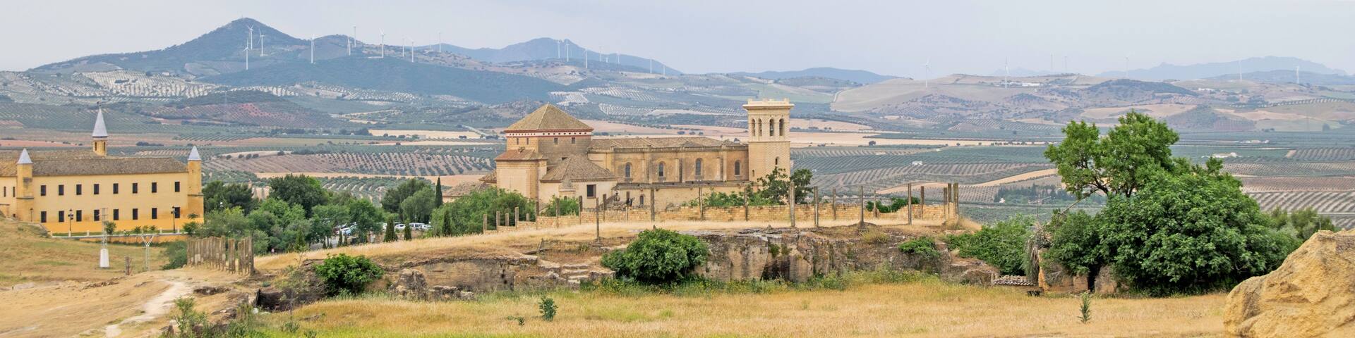 A rural landscape with a historic building, wind turbines, and terraced fields.