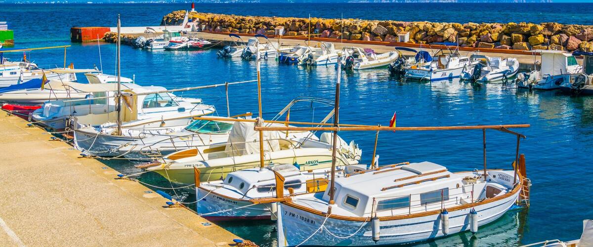 A marina with various boats docked, a rocky breakwater, and a clear blue sky.