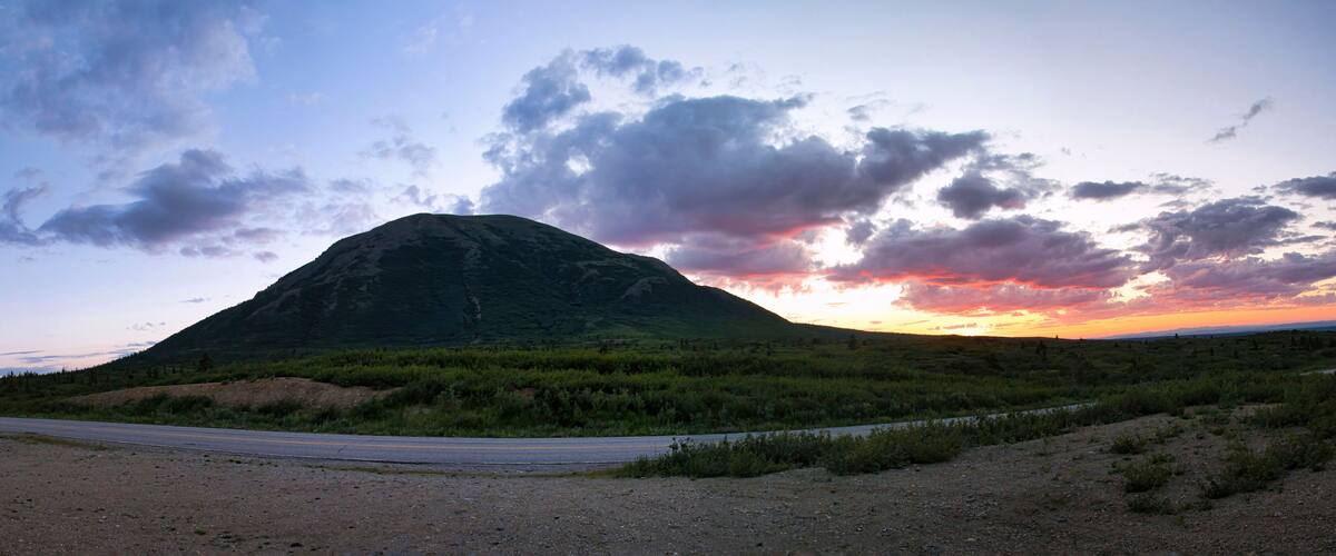 A mountain with a road in the foreground and a sunset in the background.