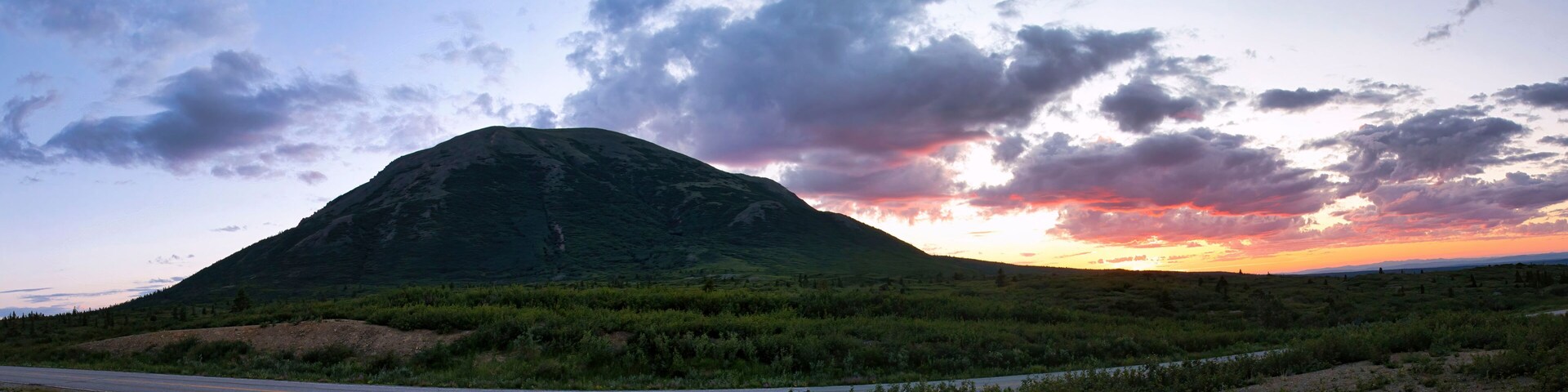 A mountain with a road in the foreground and a sunset in the background.