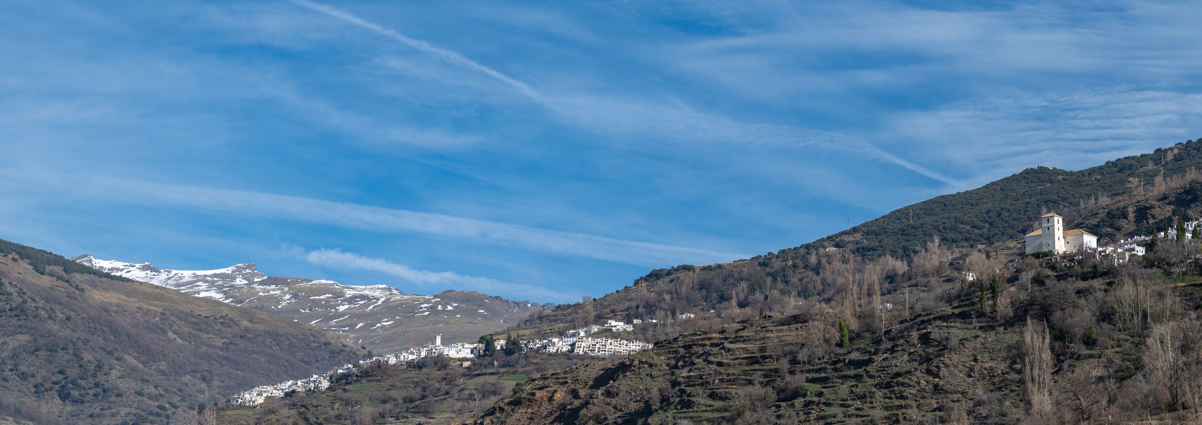 A mountainous landscape with snow-capped peaks, a village with white buildings, and a church on a hill.