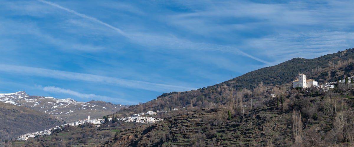 A mountainous landscape with snow-capped peaks, a village with white buildings, and a church on a hill.