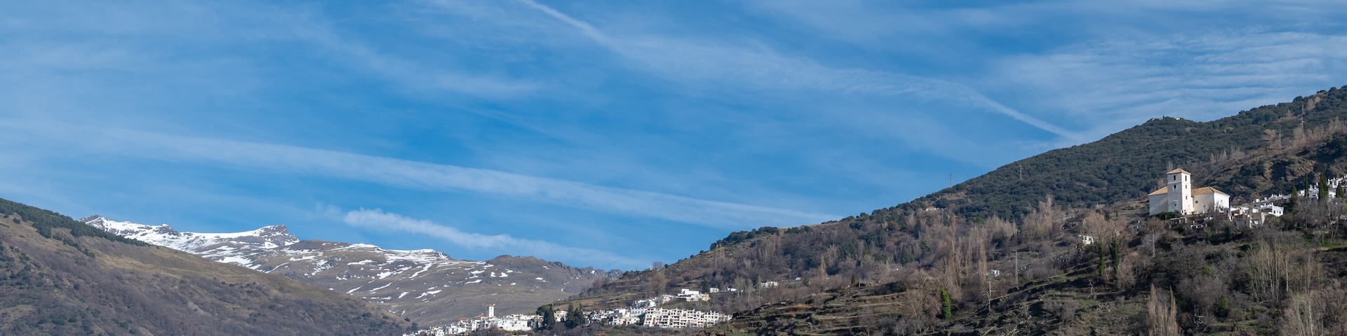 A mountainous landscape with snow-capped peaks, a village with white buildings, and a church on a hill.