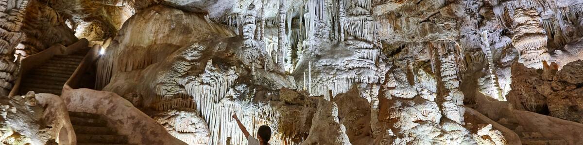 A cave with stalactites and stalagmites, a person standing on a rock, and a staircase.