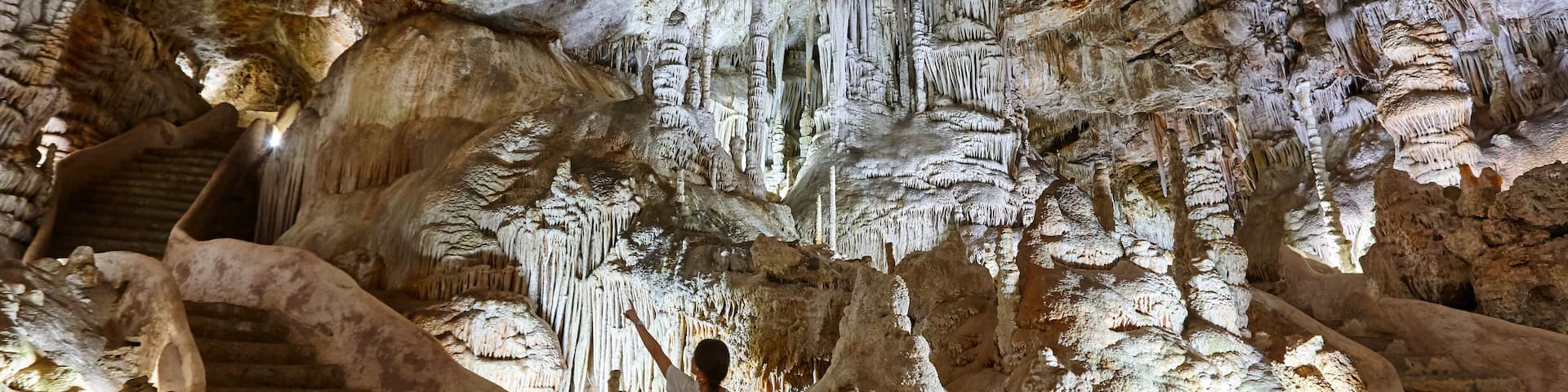 A cave with stalactites and stalagmites, a person standing on a rock, and a staircase.